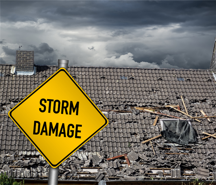Yellow sign that reads "Storm Damage" in front of a damaged roof and gray storm clouds